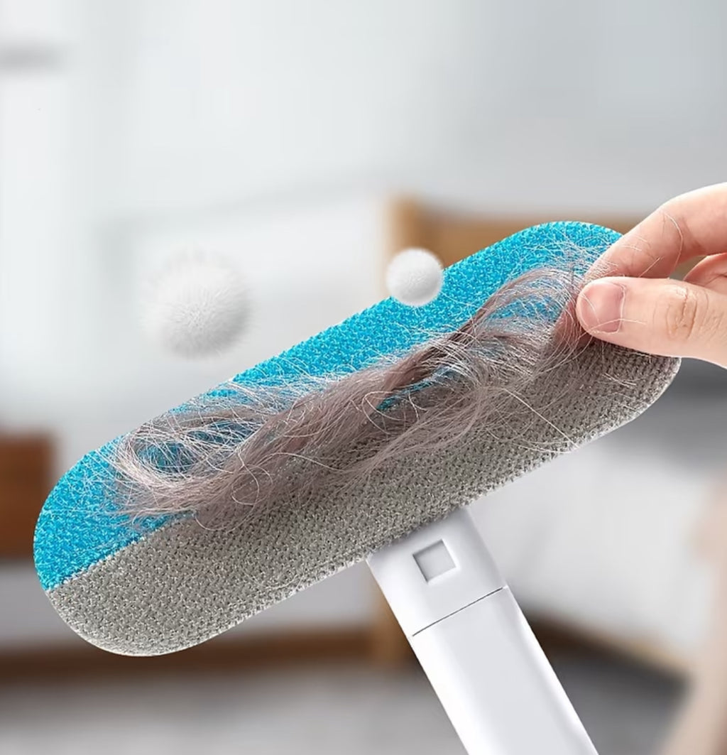 Cleaning tool with a blue sponge head covered in hair, held by a hand against a blurred indoor background.