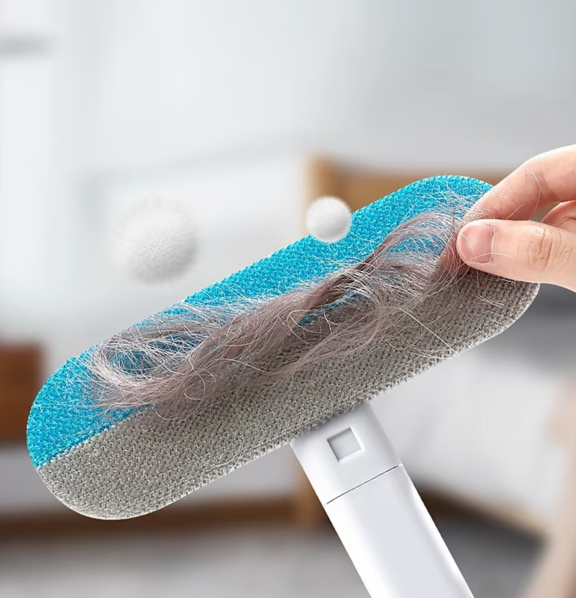 Cleaning tool with a blue sponge head covered in hair, held by a hand against a blurred indoor background.